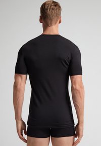 Svart kortärmad tajt t-shirt i slätt tyg, sedd bakifrån, med rundad halsringning och en lägre nederkant.