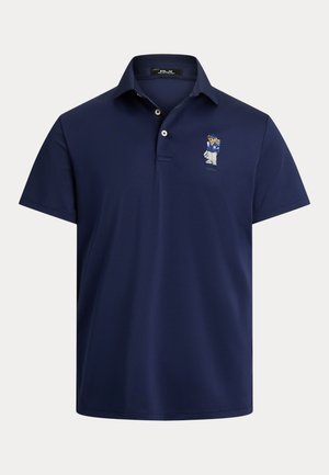 Granatowa koszulka polo z gładkiego materiału, z klasycznym kołnierzykiem i małym haftowanym logo na lewej piersi. Krótkie rękawy.