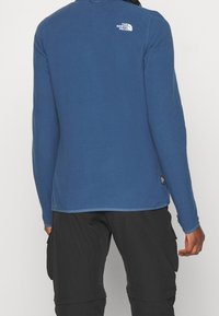 Długi rękaw polaru w ciemnoniebieskim kolorze z białym logo na plecach. Posiada okrągły dekolt oraz kontrastowe wykończenie na dole.