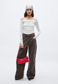 Witte top met lange mouwen en off-shoulder ontwerp, donkerbruine wijde broekspijpen en een rode handtas met een riem. Gladde texturen, eenvoudig ontwerp.