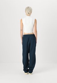 Top bianco senza maniche con colletto alto, chiusura con zip sul retro, abbinato a pantaloni larghi di colore blu navy scuro con vita elastica.