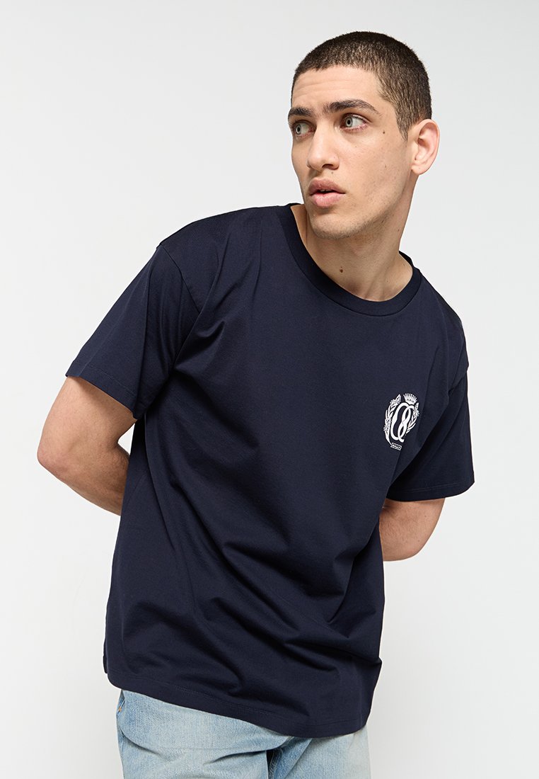 Marineblaue Baumwoll-T-Shirt mit kurzen Ärmeln, rundem Ausschnitt und einem weißen Logo auf der linken Brust. Glatte Textur und lässige Passform.