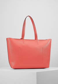 Sac fourre-tout en similicuir corail avec deux longues anses, forme structurée, coutures visibles et une poche plate à fente à l'avant.