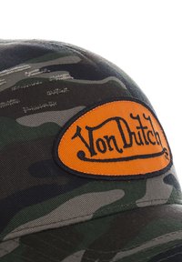 Gorra de camuflaje con una corona redondeada, que presenta un parche ovalado naranja con el logo "Von Dutch" en bordado negro. Textura de tejido de algodón.