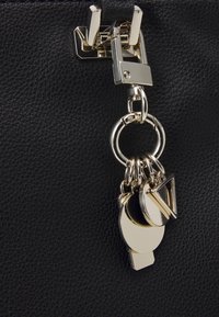 Des charms géométriques en ton or suspendus à un fermoir en or fixé à un matériau en cuir noir texturé.