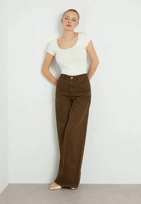 Top branco ajustado de manga curta com fecho de botão, combinado com calças castanhas de cintura alta e perna larga, com textura suave e hardware minimal.