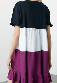 Robe à blocs de couleurs avec un haut bleu marine, une section centrale blanche et un ourlet volanté violet. Fabriquée en tissu doux avec des manches courtes volantées.