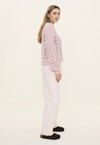 Light pink knitted sweater with openwork pattern, cropped design, and balloon sleeves. Worn over loose-fitting, pale pink pants and black footwear.