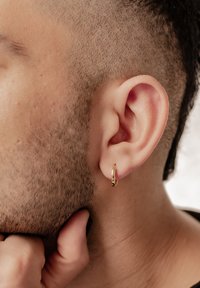 Pendiente de aro dorado visto en un primer plano de una oreja. El pendiente tiene una superficie lisa y una forma circular, complementando un cabello corto y texturizado.