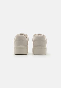 Beige sneakers with a smooth faux leather upper, padded collar, and thick rubber sole featuring embossed "TOMMY HILFIGER" branding.