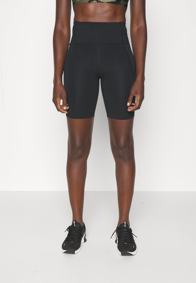 Mallas cortas deportivas negras de cintura alta con una textura suave y costuras cosidas, combinadas con zapatillas deportivas negras.