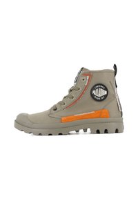 Bota alta en lona verde oliva con acentos en naranja y plata, suela de goma y parche de logo circular en el lateral. Acabado texturizado.