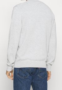 Szary sweter typu crewneck z prążkowanymi mankietami i dolnym wykończeniem, wykonany z miękkiego materiału. Sweter ma gładki krój bez wzorów.