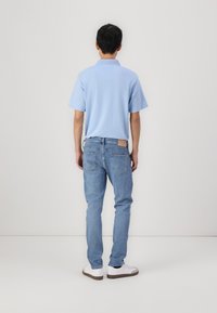 Camisa polo de color azul claro con mangas cortas, combinada con jeans de mezclilla azul claro. Los zapatos son blancos con suelas marrones. Sin patrones ni acentos visibles.