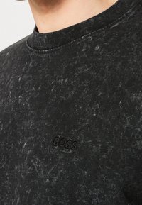 Svart crew-neck sweatshirt med en texturerad, bleknad design. Har en präglad logotyp i nedre vänstra hörnet. Mjuk tyg med ribbad halsringning.