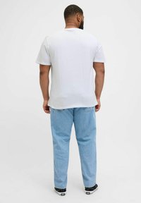 Camiseta blanca de manga corta con un corte relajado, combinada con jeans de mezclilla azul claro y zapatillas negras, vista desde atrás.