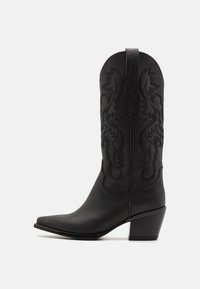 Svart cowboystøvel laget av glatt lær, med intrikat tonalt broderi, spiss tå og design med stablet hæl.