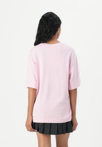 T-shirt oversize rosa chiaro con maniche corte, collo rotondo e vestibilità rilassata. Abbinato a una gonna plissettata nera. Texture liscia.