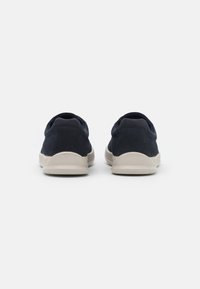 Marinblå sneakers med ett texturerat tygövre, rund tå och beige gummisula, som visar en minimalistisk design och lågprofilsilhuett.