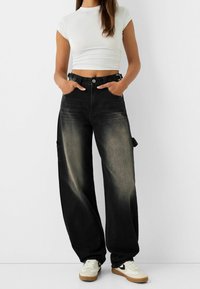 Czarne dżinsowe spodnie o szerokich nogawkach z wybledzonym wykończeniem, wysoki stan, szlufki na pasek oraz kieszenie boczne. W połączeniu z białą dopasowaną bluzką i sneakersami.