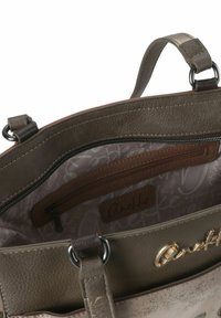 Innenraum einer grauen Handtasche aus Kunstleder mit Reißverschlusstasche und einem beigen, gemusterten Futter. Akzente aus goldfarbenen Metallteilen.