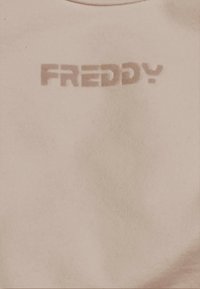 Primo piano di un tessuto beige con la parola "FREDDY" stampata in grandi lettere maiuscole e stilizzate.