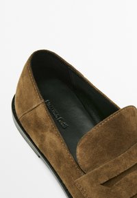 Mocassini in suede marrone con interno in pelle nera. Presentano un classico design penny e dettagli hardware minimal e lisci.