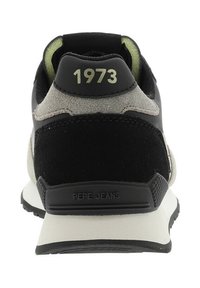 Talons de sneaker noirs, gris et beiges avec "1973" en imprimé clair et "PEPE JEANS" embossé sur le patch noir de la semelle.