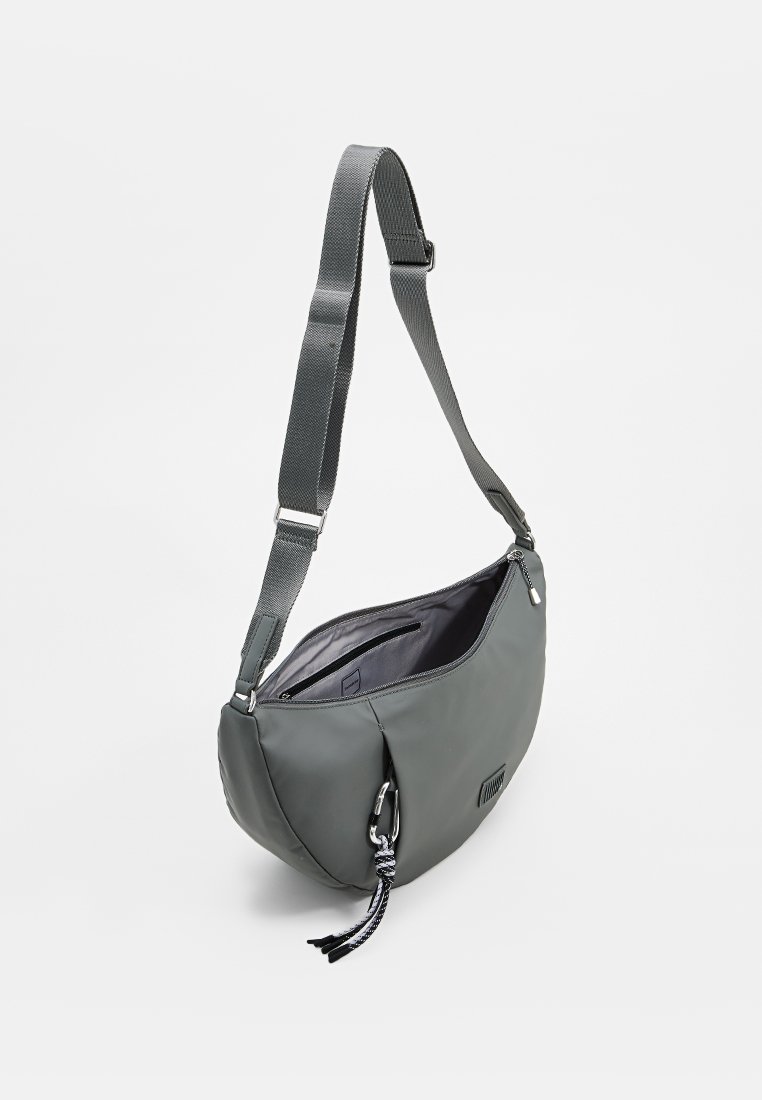 Bolso cruzado suave en gris con un acabado texturizado, correa ajustable, bolsillo con cremallera y detalle decorativo de borlas trenzadas.