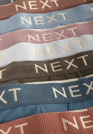 Five fabric bands in shades of brown, blue, pink, and white, featuring a ribbed texture and "NEXT" embossed in a contrasting color.