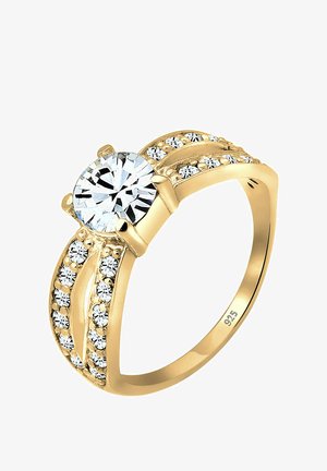 Anello d'oro con una grande gemma rotonda trasparente al centro, circondata da cristalli più piccoli lungo la fascia con una finitura liscia.