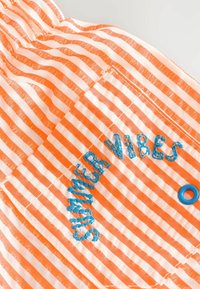Tissu rayé orange et blanc présentant un texte cousu "SUMMER VIBES" en fil bleu, avec un anneau d’accent bleu. Léger et texturé.