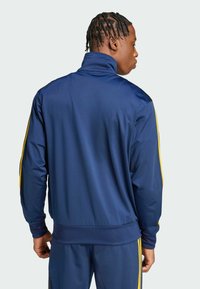 Pomorska sportska jakna s visokim ovratnikom, sa žutim bočnim trakama i glatkom teksturom, prikazana straga.