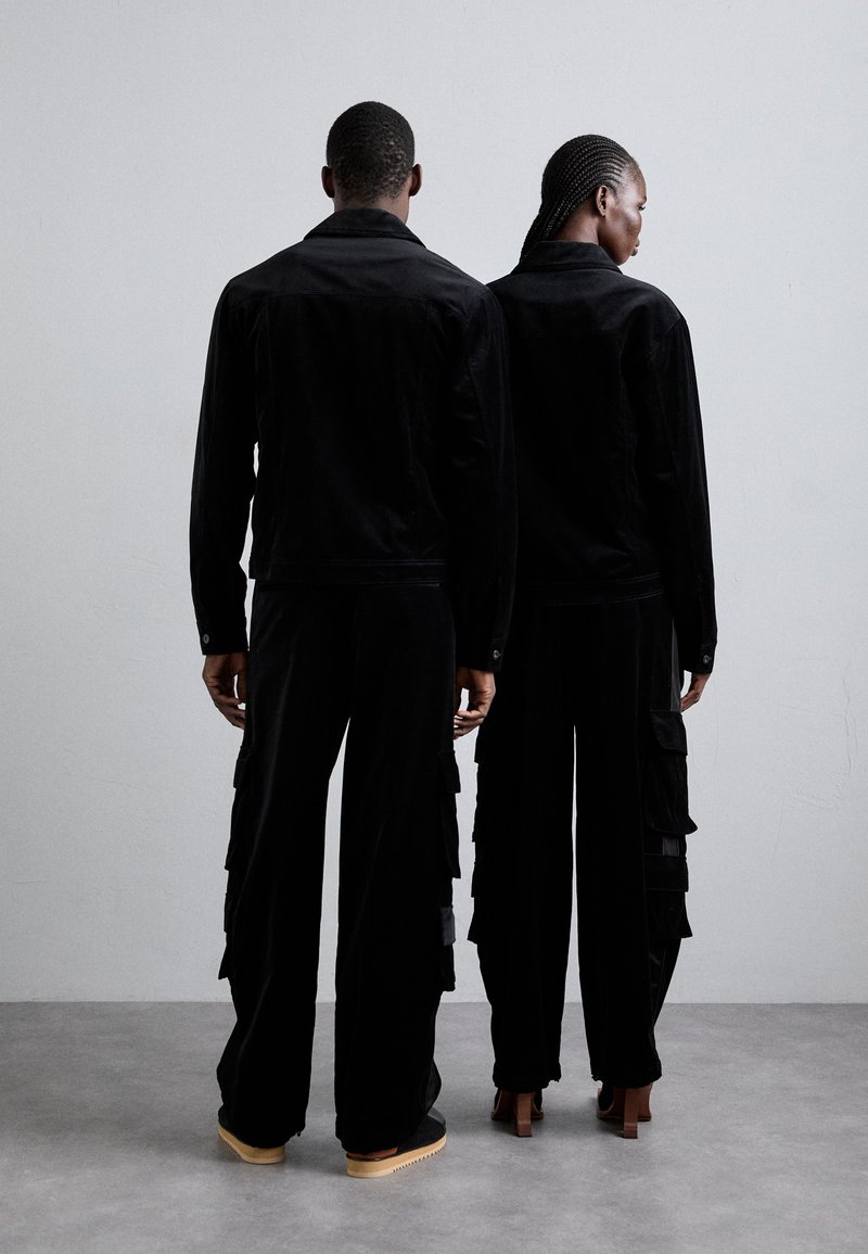 Schwarze Cordjacken und Cargo-Hosen mit aufgesetzten Taschen, die einen lockeren Sitz haben. Die Hosen bestehen aus strukturiertem Stoff und weisen Schichtelemente auf.