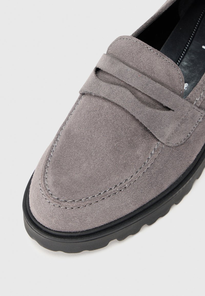 Graue Wildleder-Slipper mit schwarzer Gummisohle, dekorativem Riemen über der Oberseite und detaillierter Naht im Bereich der Zehen.