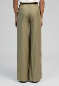 Pantalons larges de couleur vert olive clair, confectionnés dans un tissu léger et lisse ; dotés d'une taille élastique et offrant une coupe décontractée au niveau des jambes.