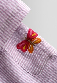 Rozā un baltas svītras audums ar nelielu izšūtu tauriņu sarkanā, oranžā, dzeltenā un rozā krāsā uz kabatas malas.