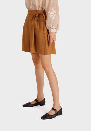 Gonna marrone di lunghezza fino al ginocchio con dettaglio in vita legato, abbinata a ballerine nere con accenti in rete e pelle.