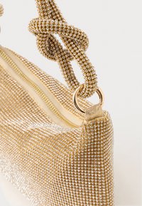 Zlata mrežasta večerna torbica z verigo, okrašeno z diamanti, in zadrgo na belem ozadju.
