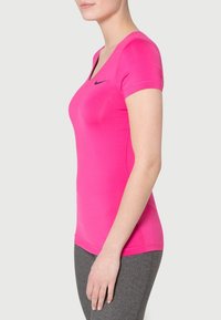 Fitted short-sleeve athletic shirt in vibrant pink fabric, featuring a v-neck and black logo detail, paired with gray leggings.