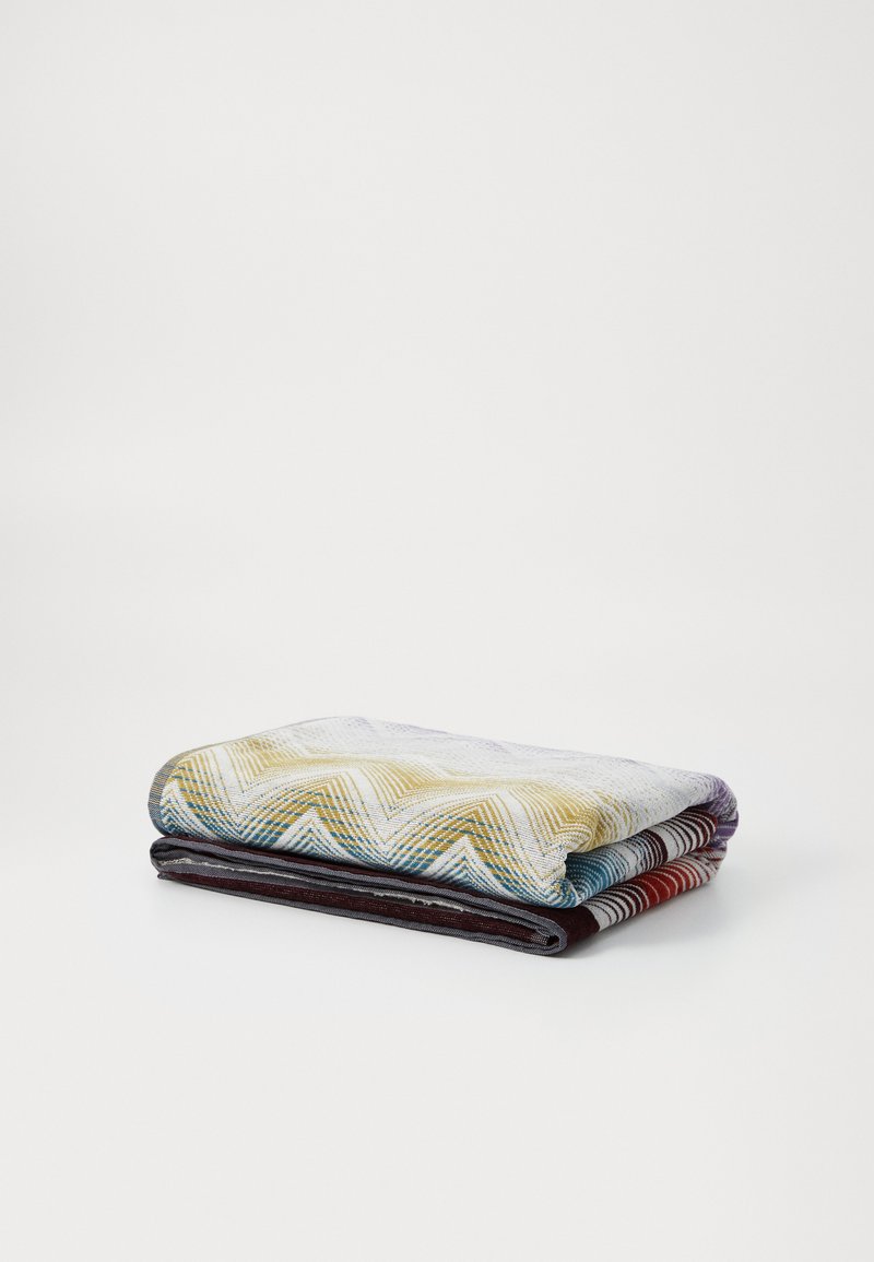 Trois couvertures en coton pliées : la première avec un motif chevron jaune, la deuxième en gris foncé, et la dernière rayée rouge et noir. Texture lisse, finition douce.