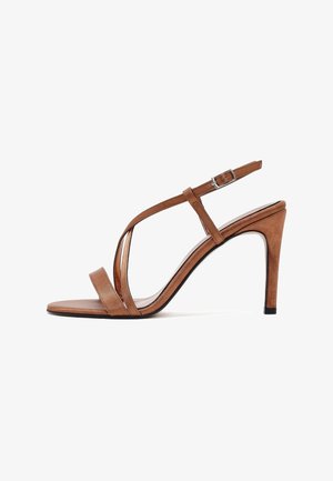 Sandale à talon haut marron avec des lanières fines, une boucle à la cheville et un talon pointu sur fond blanc.