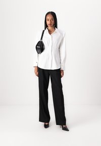 Chemise blanche à col classique avec manches longues, poignets boutonnés, coupe ajustée, pantalon noir taille haute et sac bandoulière noir.