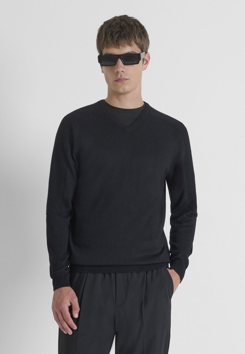 Zwarte v-hals trui met gestructureerde, ribbelachtige mouwen. Gemaakt van een zachte stof, aansluitend design. Gepaard met hoge taille zwarte broek.