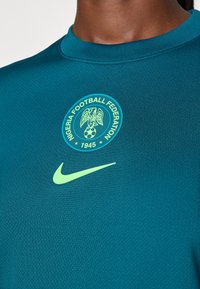 Tyrkysové športové tričko s textúrovanou tkaninou. Na hrudi má zelené logo Nike a erb Nigerijskej futbalovej federácie.