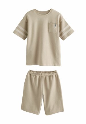 Bež srajca s kratkimi rokavi in žepom na prsih, okrašena z dvema vodoravnima črtama na rokavih, v kombinaciji z ustreznimi kratkimi hlačami z elastičnim pasom.