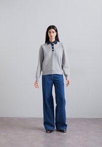 Felpa grigia con colletto e bottoni blu navy, abbinata a jeans a gamba larga blu. Tessuto liscio e vestibilità rilassata. Nessun motivo o dettaglio particolare.