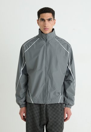 Gray windbreaker jacket with high collar, white accents, and elastic cuffs; features textured side panels for ventilation.