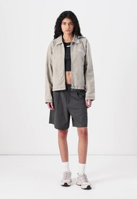 Pilkšvos spalvos zip-up striukė su apykakle, derinama su juodais languotais šortais. Papildyta lengvais batais ir baltais kojiniais, parodydama atsitiktinį stilių.