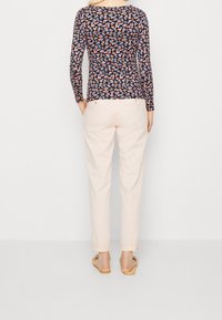 Långärmad topp med ett flerfärgat blommönster på marinblå bakgrund, kombinerad med ljusrosa byxor och platta sandaler.